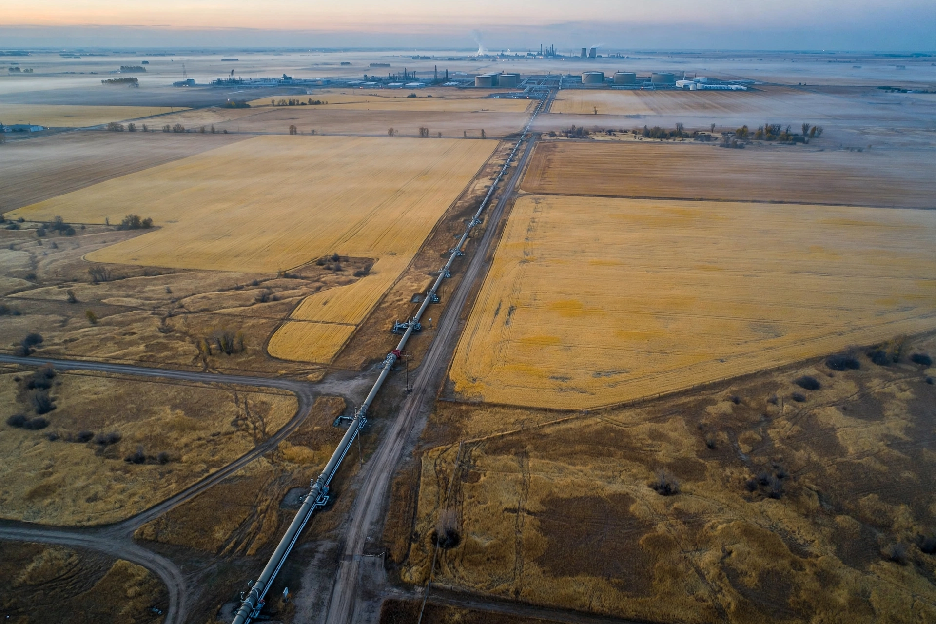 Aerial view of an oil pipeline stretching across Alberta prairie farmland at dawn
